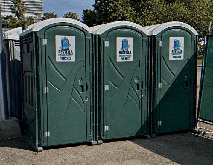 Three green portable restrooms lined up along a fence on a city work site